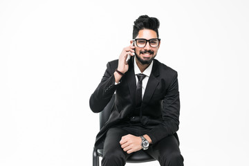 Handsome young indian businessman using mobile phone sitting on chair isolated on white background