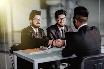 Welcome on board. Three young cheerful business people sitting together at the desk while man and woman shaking hands