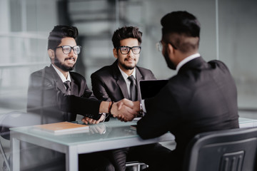 Sealing a deal. Business people shaking hands while sitting at the desk in office
