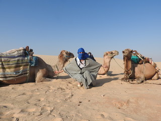 Fototapeta premium the woman in the turban, the face is closed, with a camel in the Sahara desert.