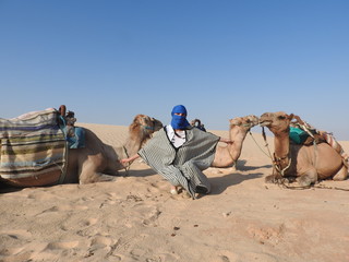 Fototapeta premium the woman in the turban, the face is closed, with a camel in the Sahara desert.