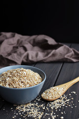 Rolled oats in bowl and spoon on dark wooden table background