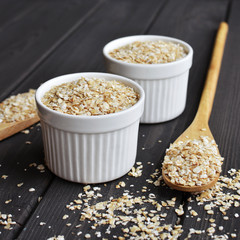 Rolled oats in bowls and spoons on dark wooden table background