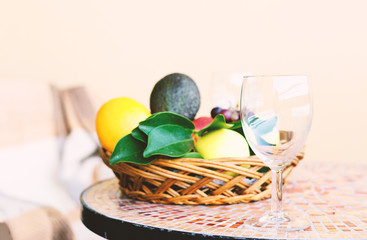 A glass and a wicker basket with fruit on a street table with a mosaic.