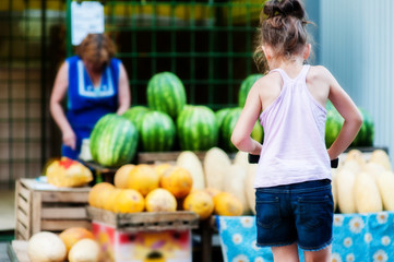 Fototapeta premium Teenager girl on a scooter stands near the counter with watermelons and melons
