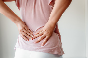 Close-Up of Woman Hands is Massaging Her Waist on Isolated Gray Background, Young Adult having Backache After Home Work. Healthcare and Medicine Concept.