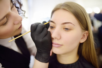 Cosmetologist painting eyebrows by brush. Attractive woman getting facial care and makeup at beauty salon. Architecture eyebrows.