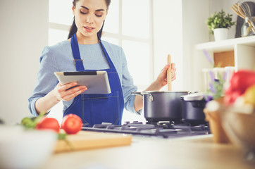 Young woman using a tablet computer to cook in her kitchen