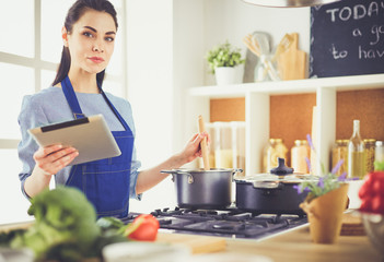 Young woman using a tablet computer to cook in her kitchen