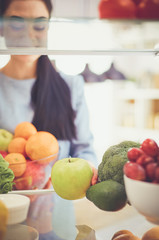 Smiling woman taking a fresh fruit out of the fridge, healthy food concept