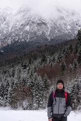 Young man hicking in the mountains during winter in the snow wearing a jacket and carrying a backpack. Active person in the cold weather