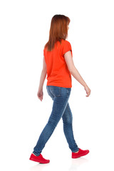 Young Woman In Orange T-Shirt, Jeans And Red Sneakers Is Walking And Looking Away