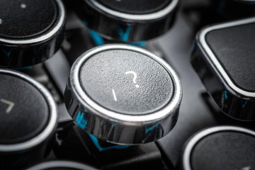 An extreme close-up or macro shot of a round slash and question mark symbols key on a vintage-inspired retro-style clicky black-and-silver metal typewriter keyboard.