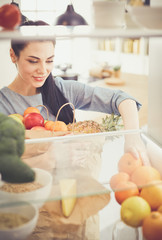 Smiling woman taking a fresh fruit out of the fridge, healthy food concept