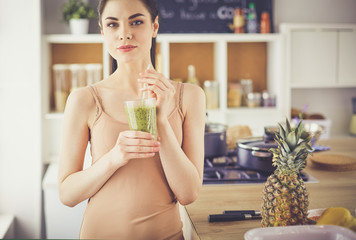 Young woman with glass of tasty healthy smoothie at table in kitchen