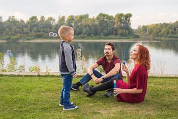 Family and nature concept - Mother, father and their child playing with colorful soap bubbles