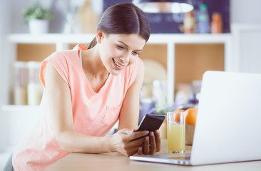 Young woman in kitchen with laptop computer looking recipes, smiling. Food blogger concept.