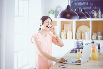 Young woman in kitchen with laptop computer looking recipes, smiling. Food blogger concept.