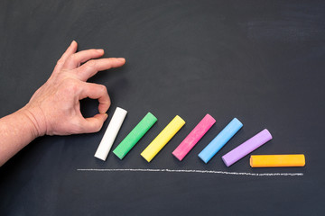 colored chalk in male hand on the background of chalk board