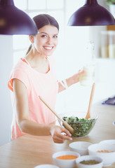 Smiling young woman mixing fresh salad in the kitchen.