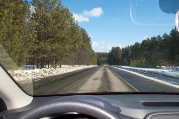 View of the road through the windshield. Snow on the sidelines. Wet asphalt road. Blue sky with...