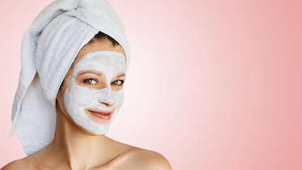 Beautiful young woman with facial mask on her face. Skin care and treatment, spa, natural beauty and cosmetology concept.