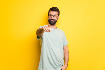 Man with beard and green shirt points finger at you with a confident expression - obrazy, fototapety, plakaty