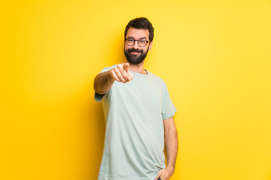 Man with beard and green shirt points finger at you with a confident expression