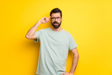 Man with beard and green shirt making the gesture of madness putting finger on the head