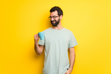 Man with beard and green shirt holding a hot cup of coffee