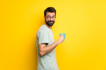 Man with beard and green shirt holding a hot cup of coffee