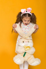 Portrait of cute little child girl with Easter bunny ears holding bunny on yellow background. Happy easter