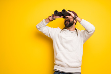 Hippie man with dreadlocks and looking in the distance with binoculars