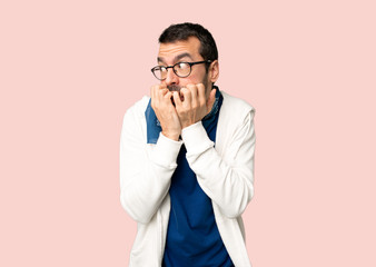 Handsome man with glasses is a little bit nervous and scared putting hands to mouth on isolated pink background