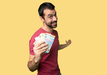 Man taking a lot of money pointing back and presenting a product on isolated yellow background
