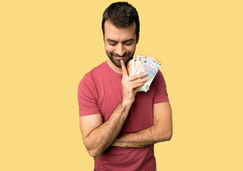 Man taking a lot of money looking down with the hand on the chin on isolated yellow background