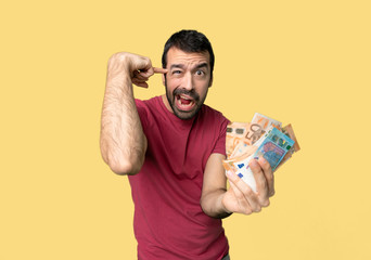 Man taking a lot of money making the gesture of madness putting finger on the head on isolated...