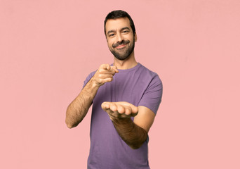 Handsome man holding copyspace imaginary on the palm to insert an ad on isolated pink background