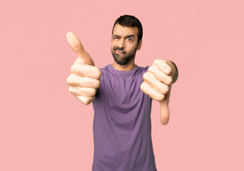 Handsome man making good-bad sign. Undecided between yes or not on isolated pink background