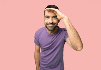 Handsome man looking far away with hand to look something on isolated pink background