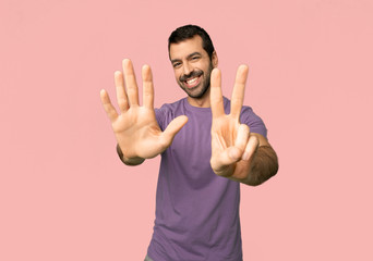 Handsome man counting seven with fingers on isolated pink background