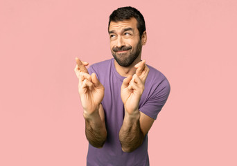 Fototapeta premium Handsome man with fingers crossing and wishing the best on isolated pink background