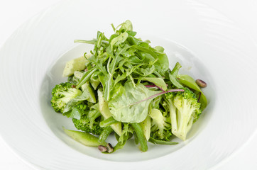 Salad of green vegetables with broccoli, zucchini and walnut dressing on a plate on a white background