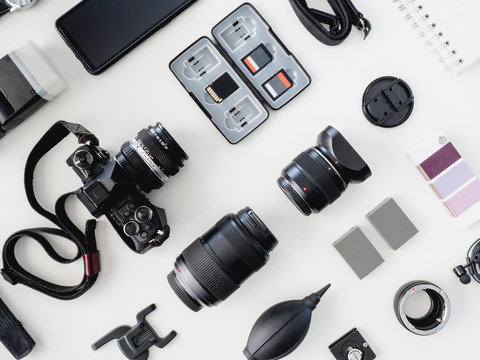 top view of work space photographer with digital camera, flash, cleaning kit and memory card on white table background.