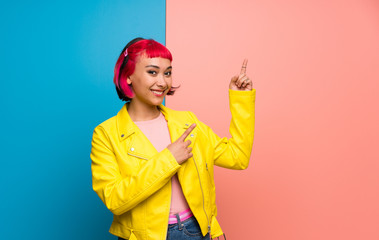 Young woman with yellow jacket pointing with the index finger and looking up