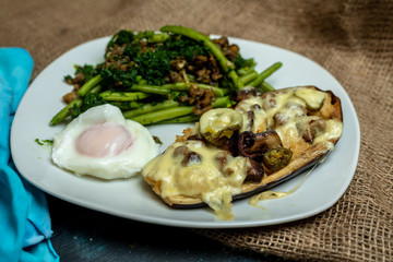 Baked eggplant with cheese and mushrooms, next to green legumes and spinach and fried egg