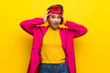 Young woman with pink hair over yellow wall frustrated and takes hands on head