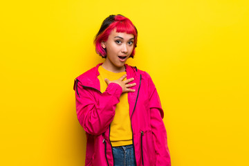 Young woman with pink hair over yellow wall surprised and shocked while looking right