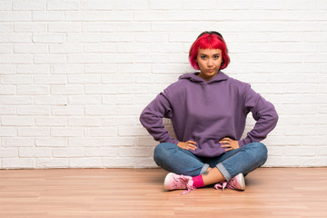 Young woman with pink hair sitting on the floor angry