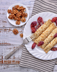 Pancakes, Walnut and Plums. Pancakes with filling on a white plate. Wood background. Rustic style. Rolled up pancakes. Wrapped thin pancakes. Homemade crepes, dried fruits, nuts.